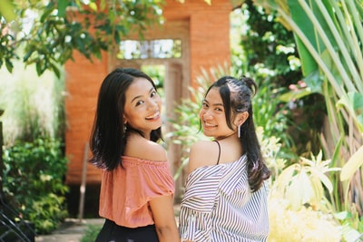 The two women stood next to the green plants during the day
